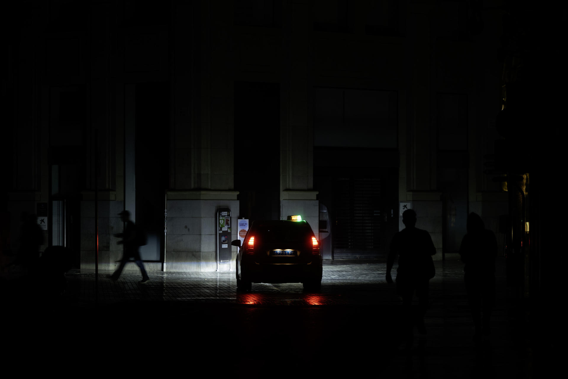 Personas caminan a oscuras por una calle andaluza, iluminada solo por los faros de un coche, durante el apagón del 28 de abril de 2025. EFE/ Jorge Zapata