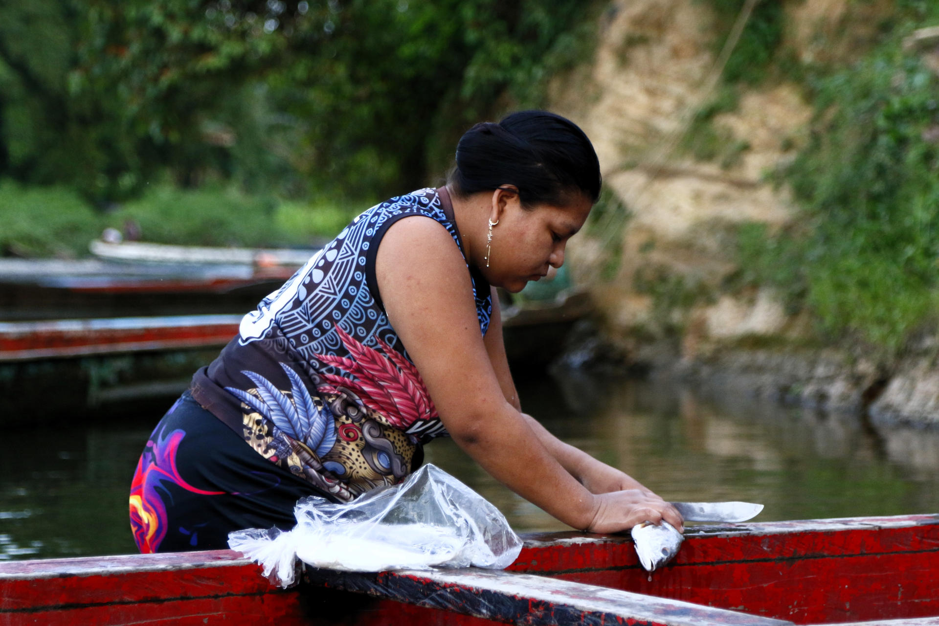 Una indígena limpia pescado en la orilla del río Tuquesa el 18 de junio de 2025, en el poblado de Bajo Chiquito, cerca de la selva del Darién (Panamá). EFE/Moncho Torres