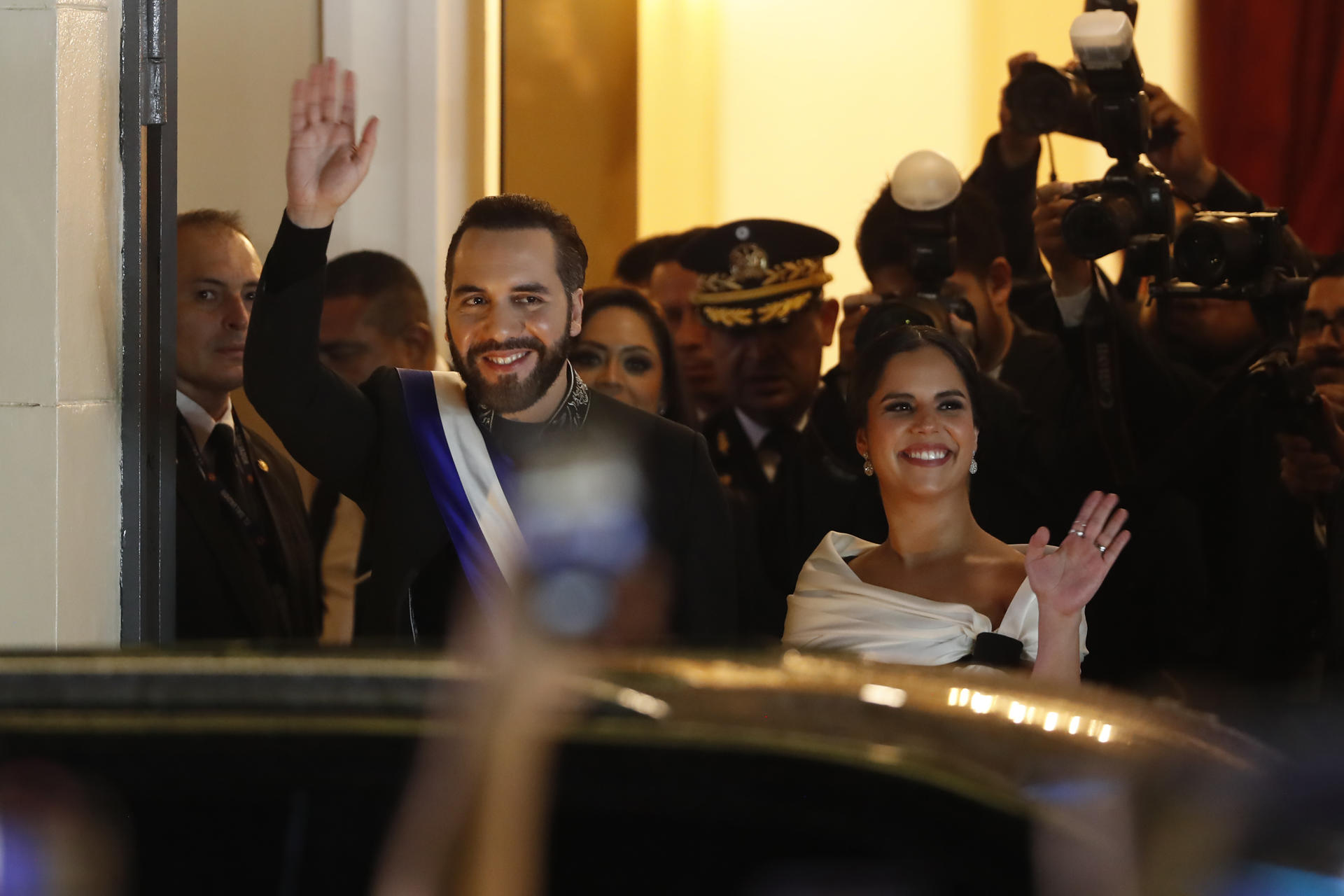 El presidente de El Salvador, Nayib Bukele, y su esposa Gabriela Rodríguez saludan este domingo, a las afueras del Teatro Nacional en San Salvador (El Salvador). Bukele aseguró en su discurso por el primer año de su segundo mandato consecutivo, que "le tiene sin cuidado que le llamen dictador" y que prefiere eso "a ver cómo matan a los salvadoreños". EFE/ Rodrigo Sura
