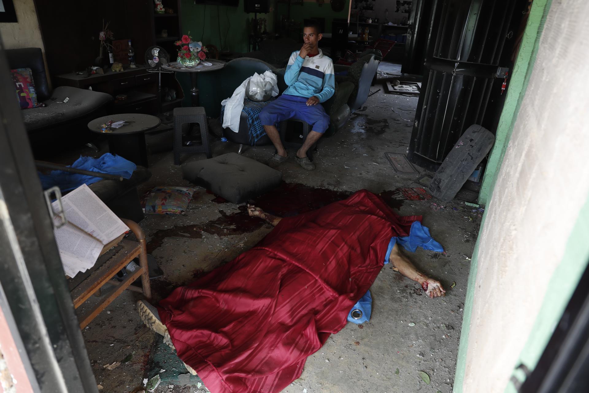 Un hombre espera al lado del cuerpo sin vida de una persona después de una explosión este martes en Guachinte, Jamundí (Colombia). EFE/Ernesto Guzmán