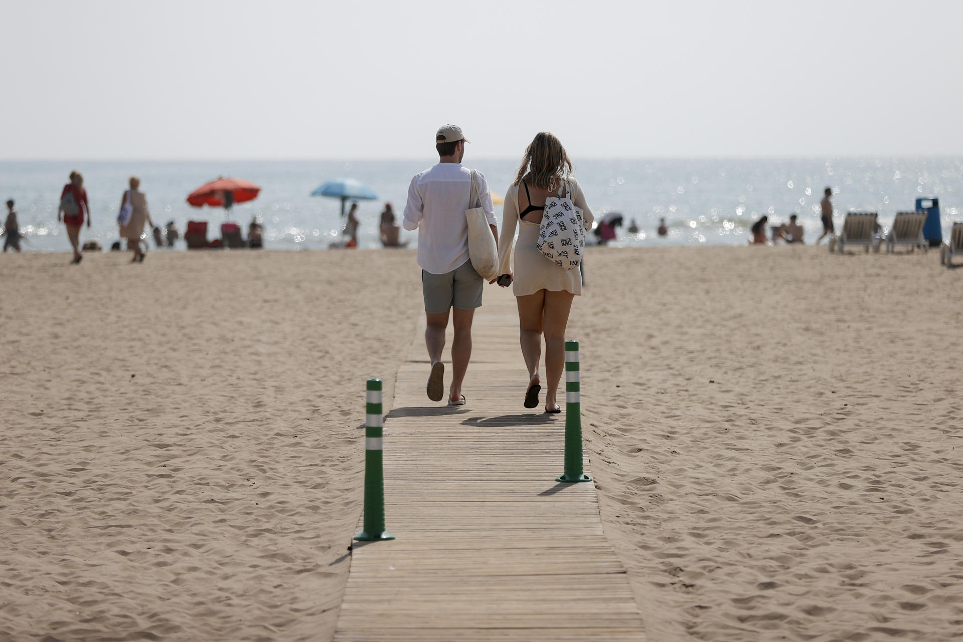 Dos personas pasean por la playa de la Malvarrosa durante la mañana de este martes en el que toda la península, salvo la franja norte y buena parte del litoral -diez comunidades en concreto- están en aviso por calor, lluvias y tormentas con posibilidad de fuerte viento y granizo, y de ellas cinco se encuentran en nivel de riesgo naranja (importante), con temperaturas de hasta 41 grados en Andalucía. EFE/Manuel Bruque