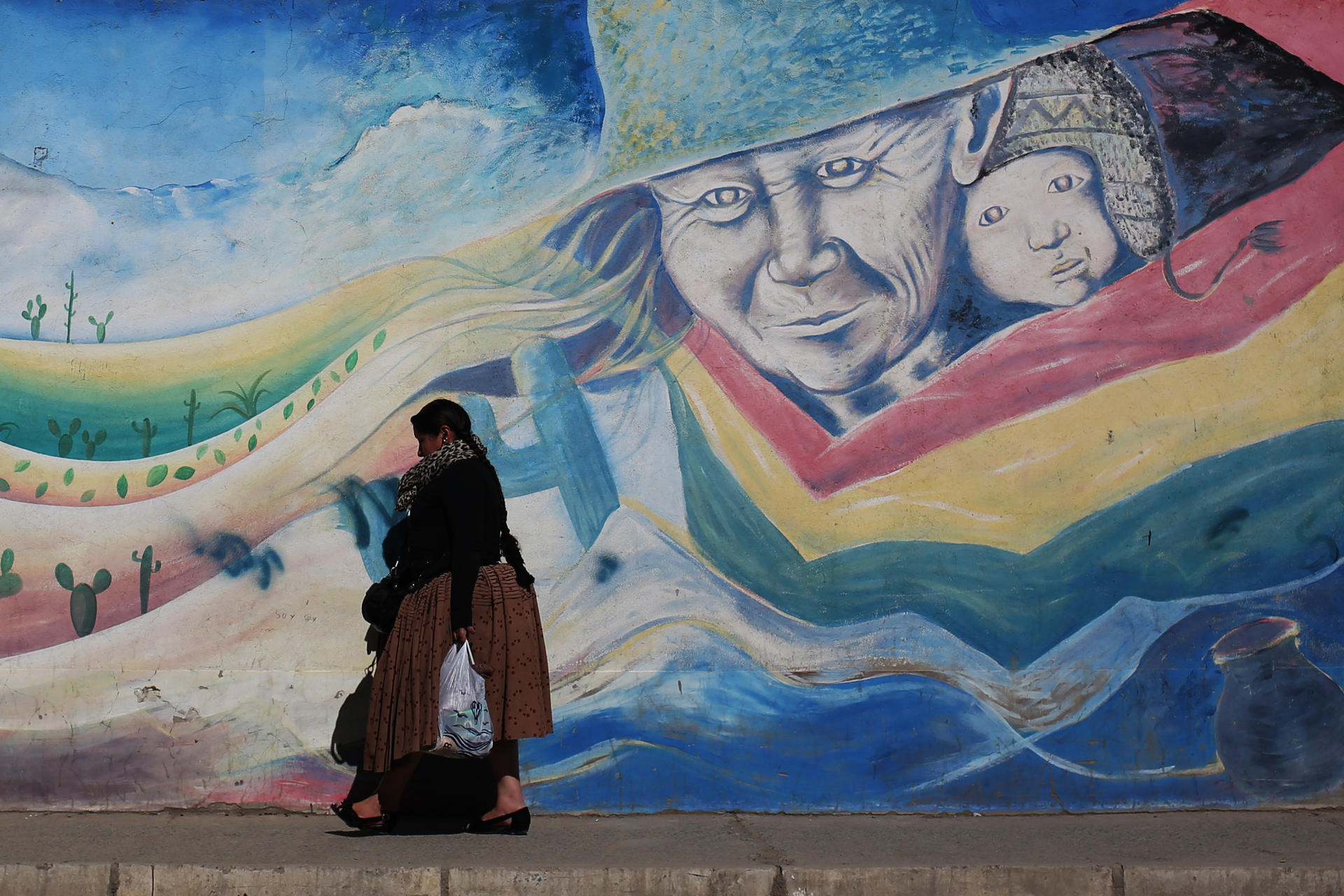 Una mujer aimara camina frente a un mural este martes, en El Alto (Bolivia). EFE/ Luis Gandarillas