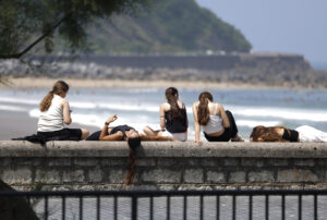 Unas jóvenes toman el sol junto a la playa de la Zurriola de San Sebastián este viernes. EFE/Juan Herrero.