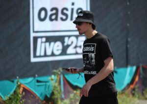 Un seguidor de Oasis pasa por delante de un cartel anunciador de su gira este 4 de julio en Cardiff. EFE/EPA/ADAM VAUGHAN