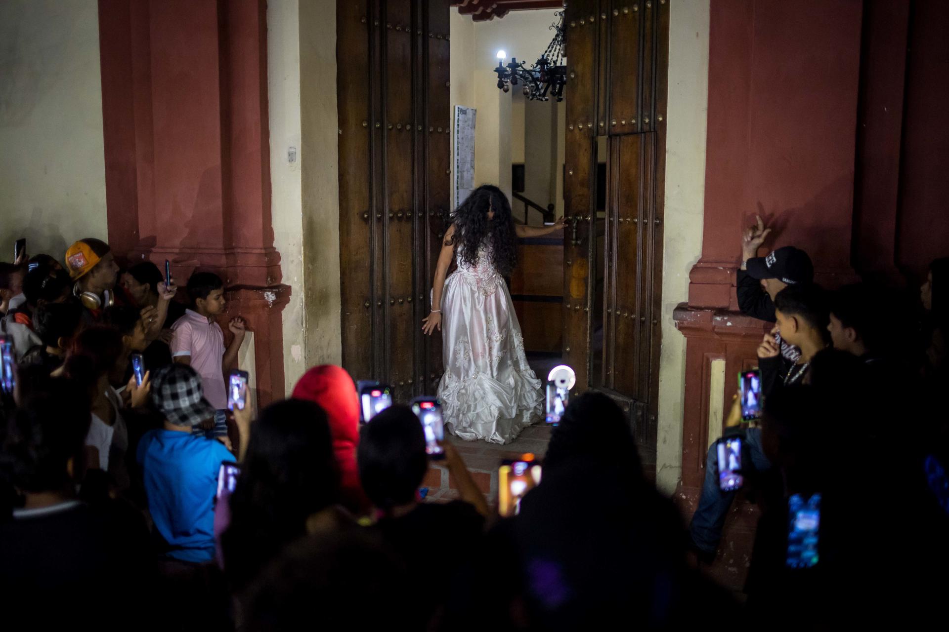 Personas observan a una actriz durante la actividad 'Ruta del Terror´ este miércoles, en la zona colonial de Petare, en Caracas (Venezuela). EFE/ Miguel Gutiérrez

