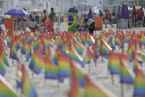 Unas personas permanecen en la playa cerca a banderas alusivas al movimiento LGBTI durante una protesta este domingo en la playa de Ipanema, en Río de Janeiro (Brasil). EFE/ Andre Coelho