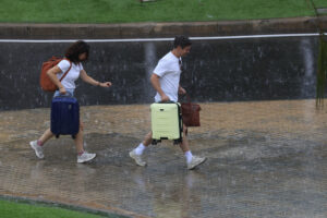 Dos personas con equipaje caminan bajo la lluvia en el aeropuerto de Manises (València). EFE/ Kai Forsterling