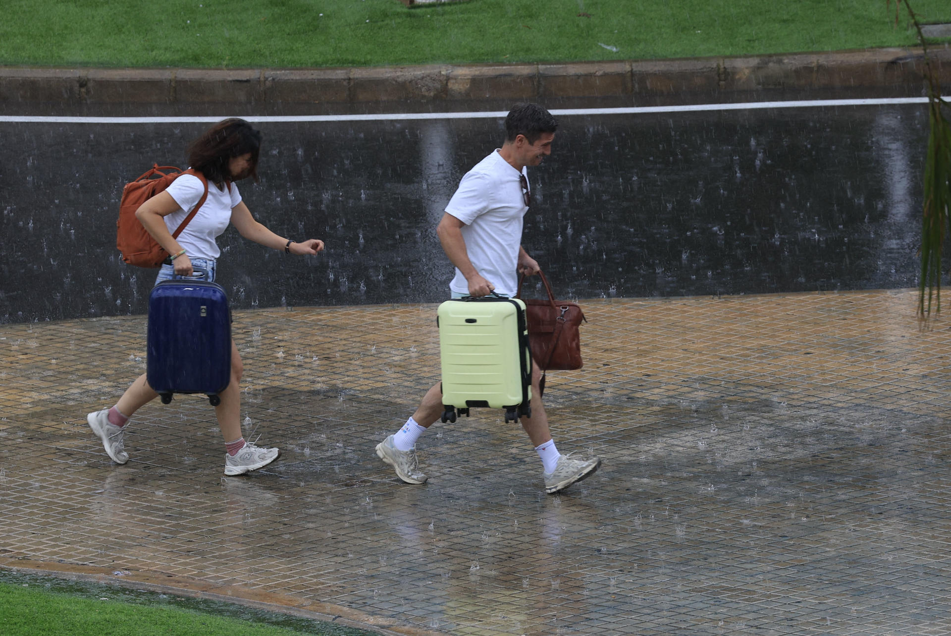 Dos personas con equipaje caminan bajo la lluvia en el aeropuerto de Manises (València). EFE/ Kai Forsterling