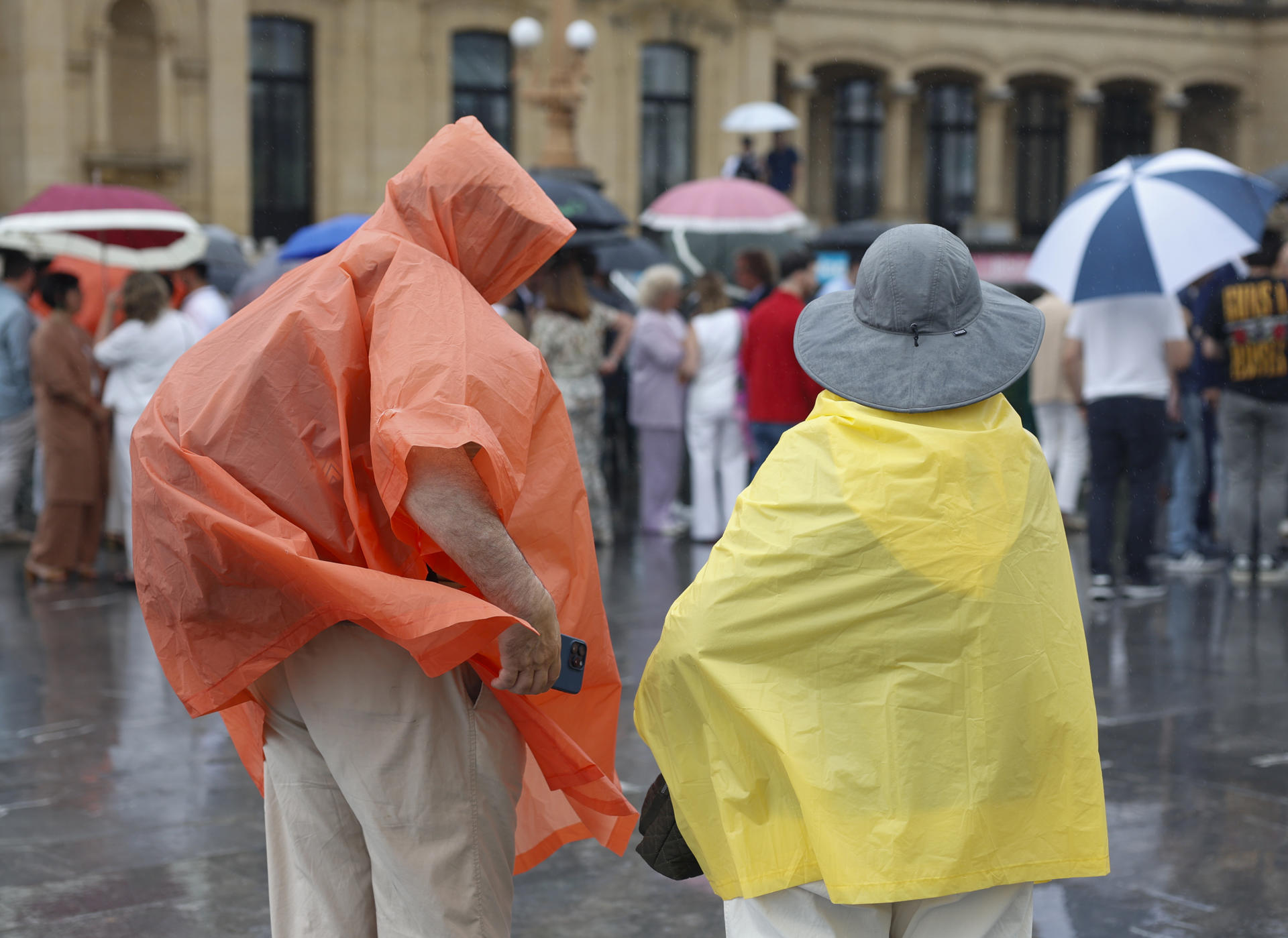 Unos turistas se protegen de la lluvia con chubasqueros este miércoles San Sebastián. EFE/Juan Herrero
