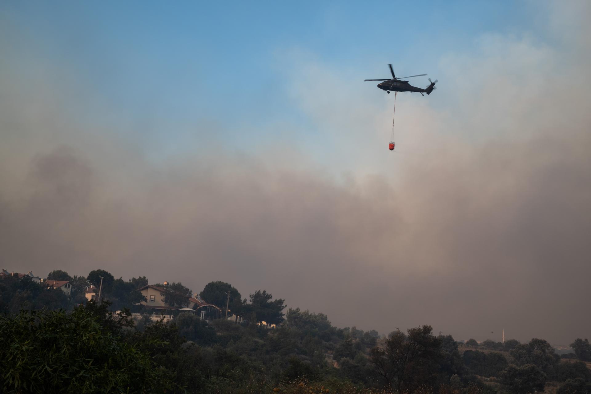 Un helicóptero transporta agua para apagar el fuego durante los incendios forestales en el distrito de Seferihisar este lunes, en de Izmir (Turquía). EFE/EPA/ Murat Kocabas