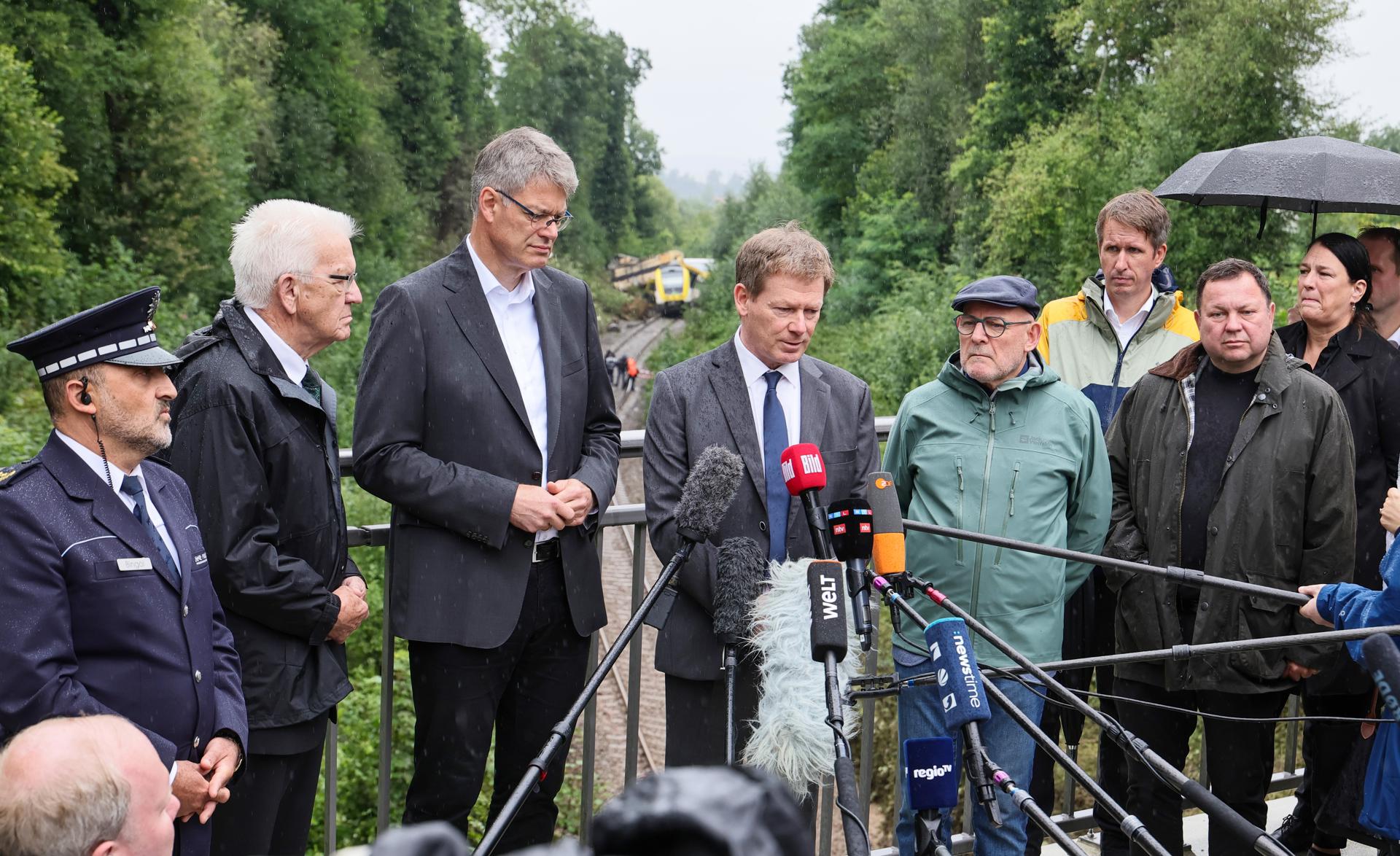 El ministro-presidente de Baden-Wuerttemberg Winfried Kretschmann (2-i), el ministro federal de Transporte de Alemania, Patrick Schnieder (3-i), y el presidente de Deutsche Bahn, Richard Lutz (4-i) hablan con los medios este lunes en el lugar del accidente en el que un tren de pasajeros descarriló este domingo y provocó la muerte de tres personas, cerca de Riedlingen (Alemania). EFE/EPA/RONALD WITTEK
