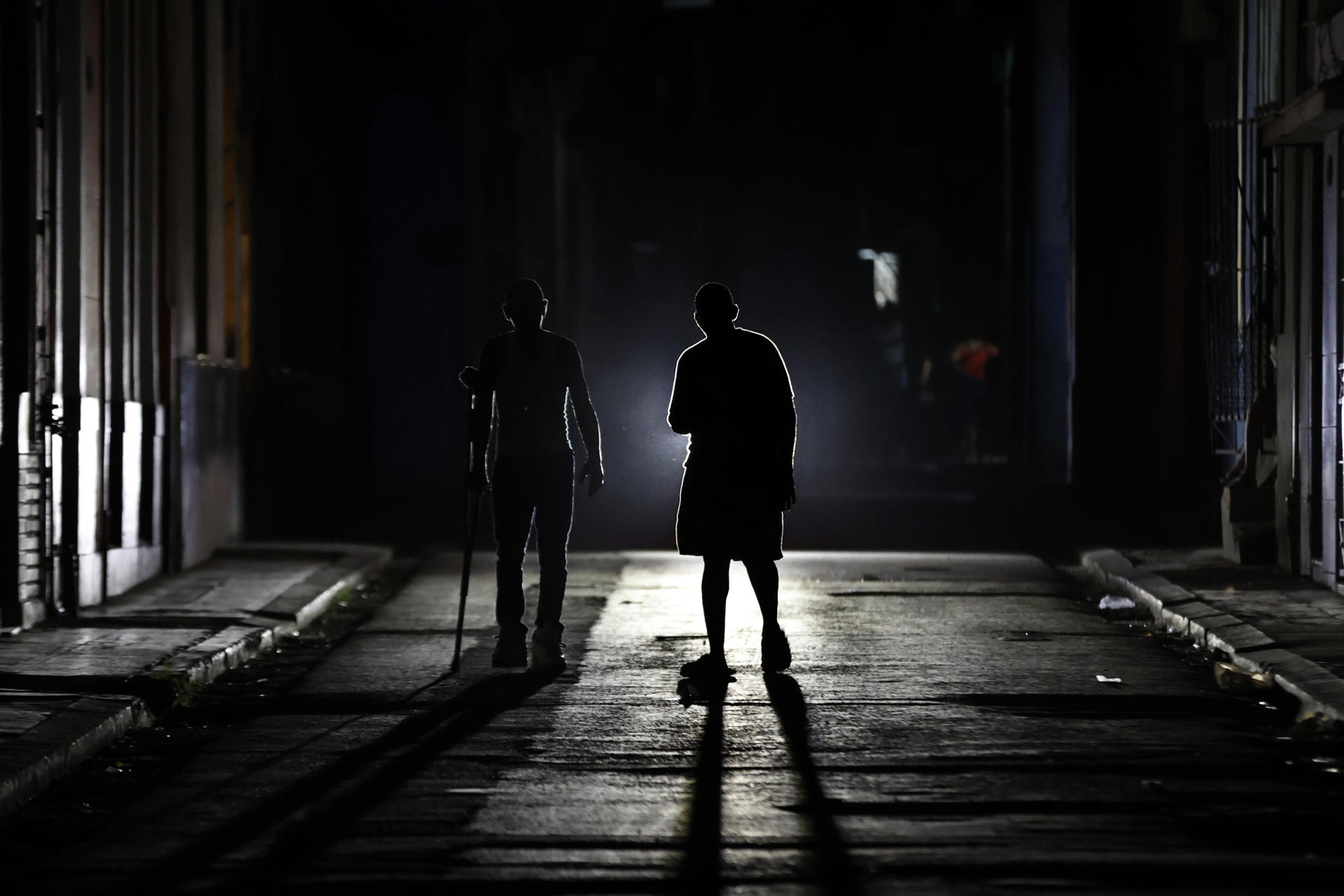 Un par de personas fue captado la madrugada del 1 de julio al caminar por una calle en penumbra, durante uno de los diarios apagones eléctricos, en La Habana (Cuba). EFE/Ernesto Mastrascusa