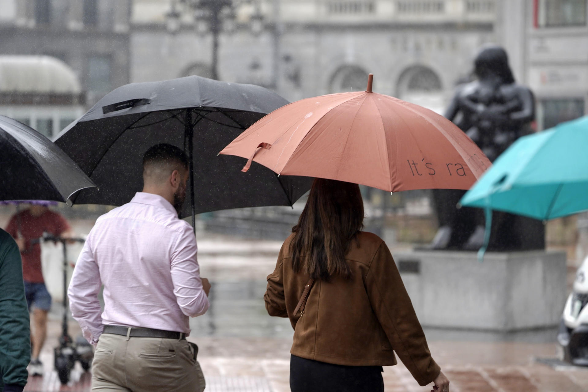 Viandantes con paraguas protegiéndose de la lluvia en el centro de Oviedo, este viernes. EFE/Paco Paredes
