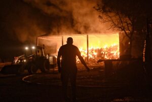 Bomberos y voluntarios combaten un almacén en llamas durante un incendio forestal en la aldea de Feneos, municipio de Corinto, Grecia, este miércoles. EFE/ EPA/ANA-MPA/Vassilis Psomas