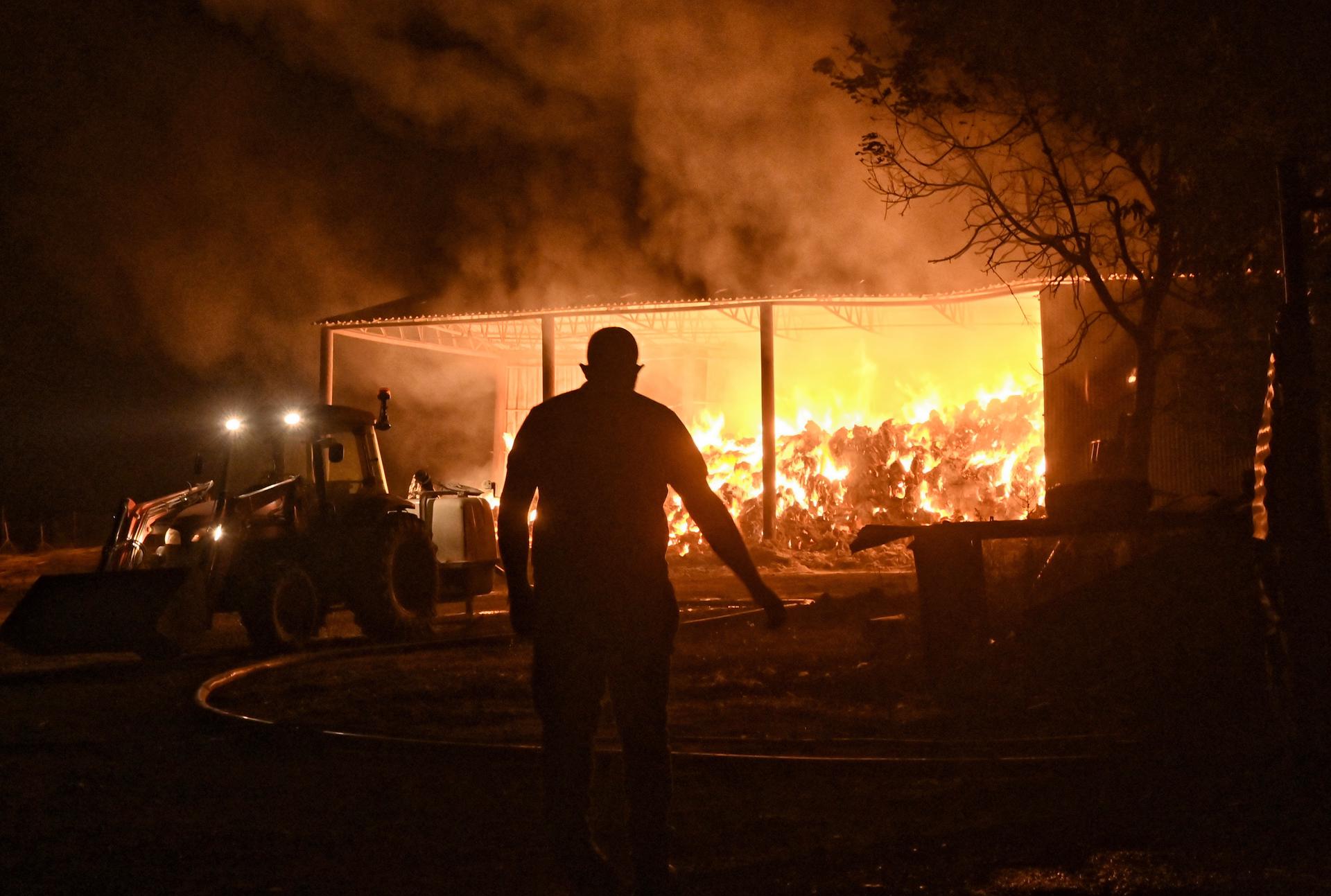 Bomberos y voluntarios combaten un almacén en llamas durante un incendio forestal en la aldea de Feneos, municipio de Corinto, Grecia, este miércoles. EFE/ EPA/ANA-MPA/Vassilis Psomas