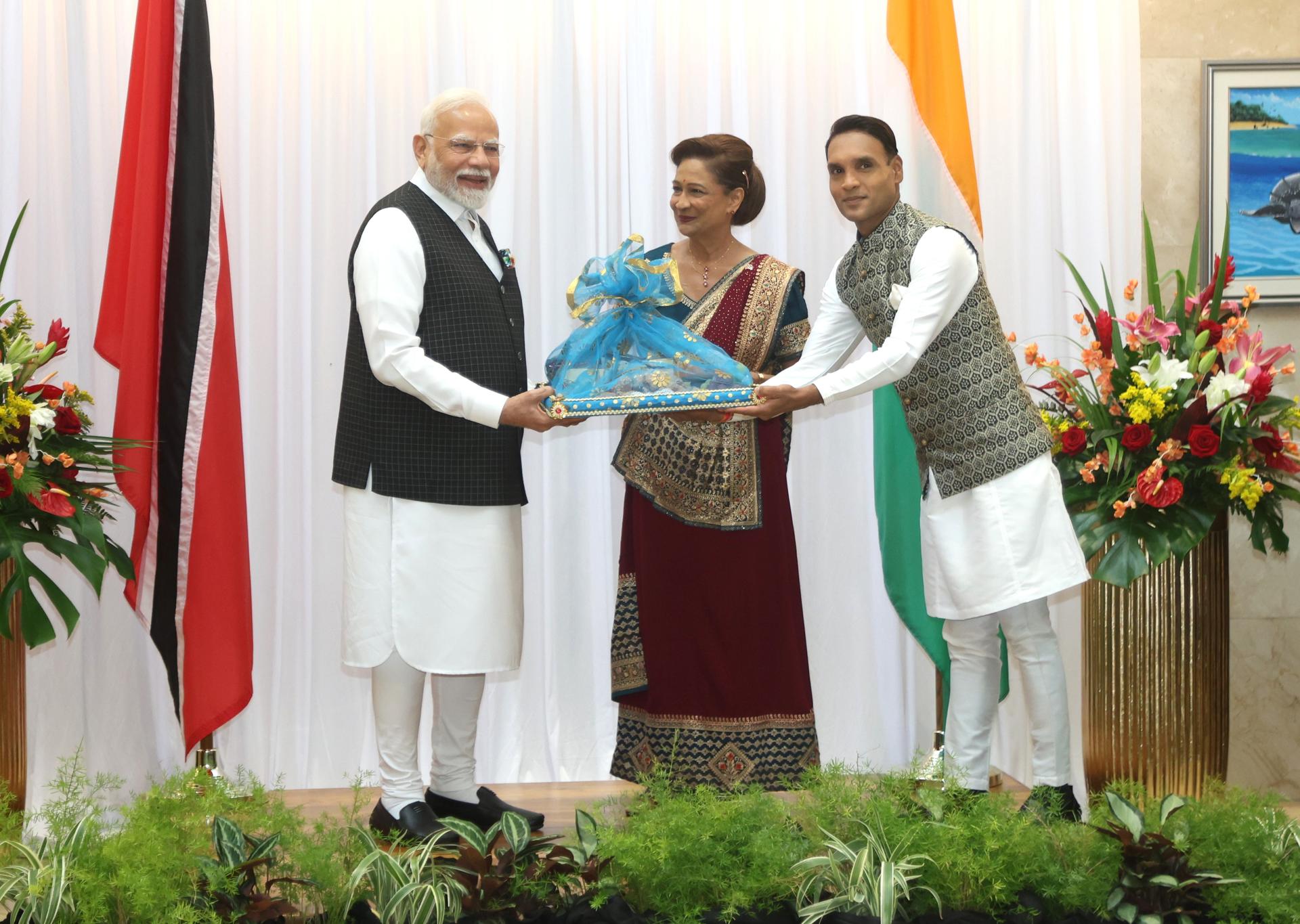 El primer ministro de la India, Narendra Modi (i), recibe dulces indios de manos de su homóloga de Trinidad y Tobago, Kamla Persad-Bissessar (c), y el ministro asistente Barry Padarath (d), este viernes en la Casa Roja de Puerto España (Trinidad y Tobago). Modi finalizó una visita de Estado de dos días a Trinidad y Tobago haciendo un llamamiento a la colaboración para "dar al sur global el lugar que le corresponde". EFE/Karla Ramoo