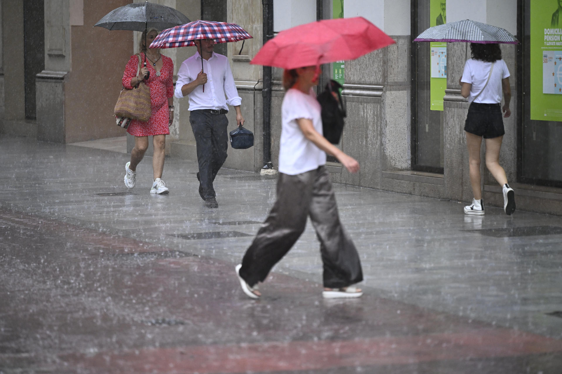 Varias personas caminan este miércoles por una calle de la ciudad de Castellón bajo una intensa lluvia. EFE/Andreu Esteban