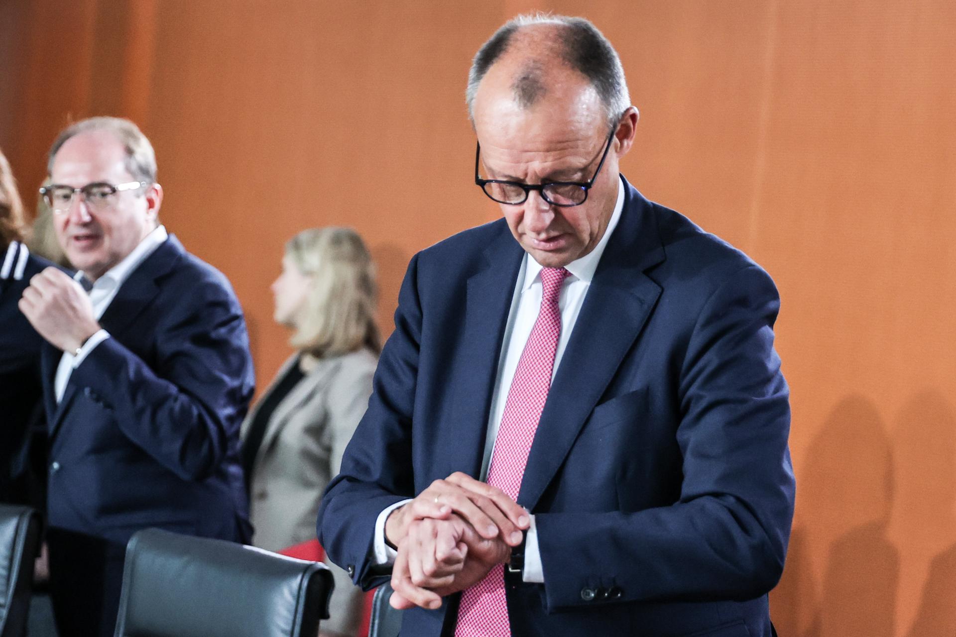Friedrich Merz (derecha) mira su reloj mientras asiste a la reunión del gabinete federal en la Cancillería en Berlín, Alemania, el 23 de julio de 2025. (Alemania) EFE/EPA/FILIP SINGER