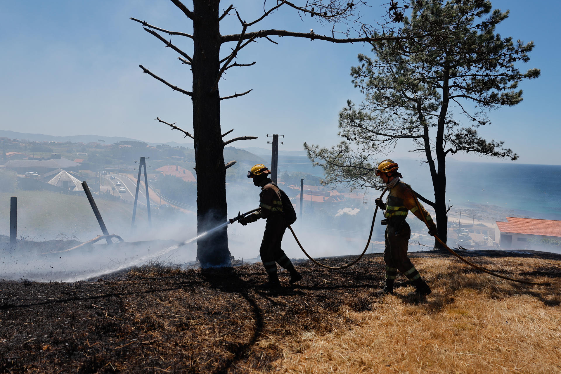Bomberos trabajan este martes, en la extinción de un incendio en A Lanzada (Pontevedra). EFE/ Lavandeira Jr