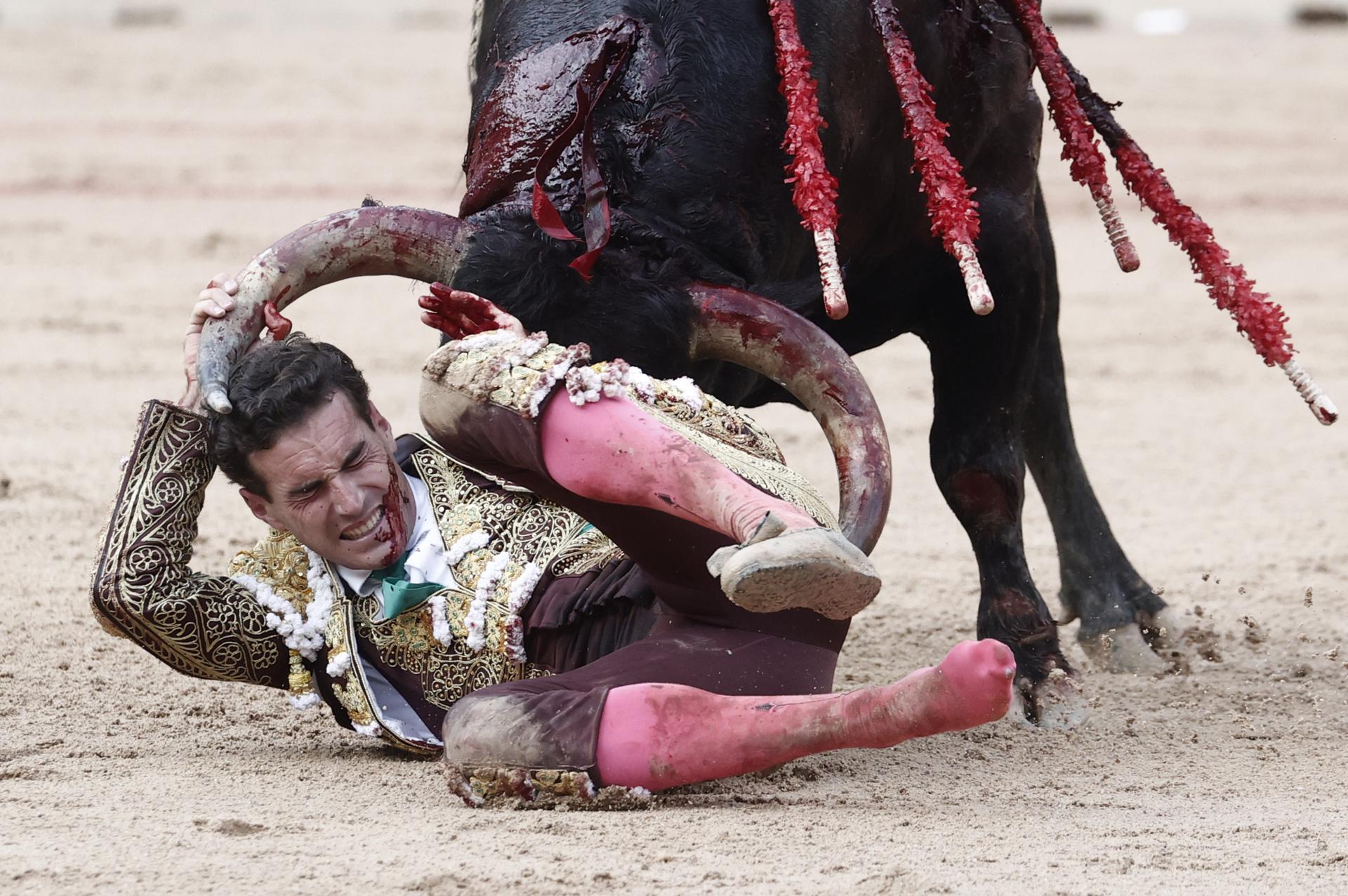 El torero Fernando Adrián sufre un revolcón durante la lidia a su segundo toro de la tarde en la novena de abono de la Feria de Toro de los Sanfermines 2025 con toros de la ganadería gaditana La Palmosilla y en la que comparte cartel con los diestros Jiménez Fortes y Ginés Marín. EFE/Jesús Diges