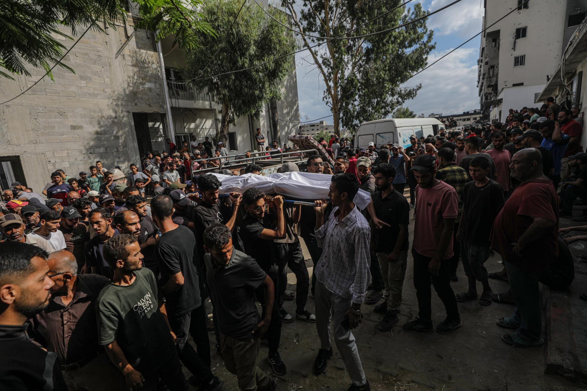 Palestinos desplazados internamente llevan el cuerpo de un joven fuera del Hospital Al Shifa después de que fuera asesinado a tiros en un punto de distribución de alimentos cerca de Zikim, en la Ciudad de Gaza. EFE/MOHAMMED SABER