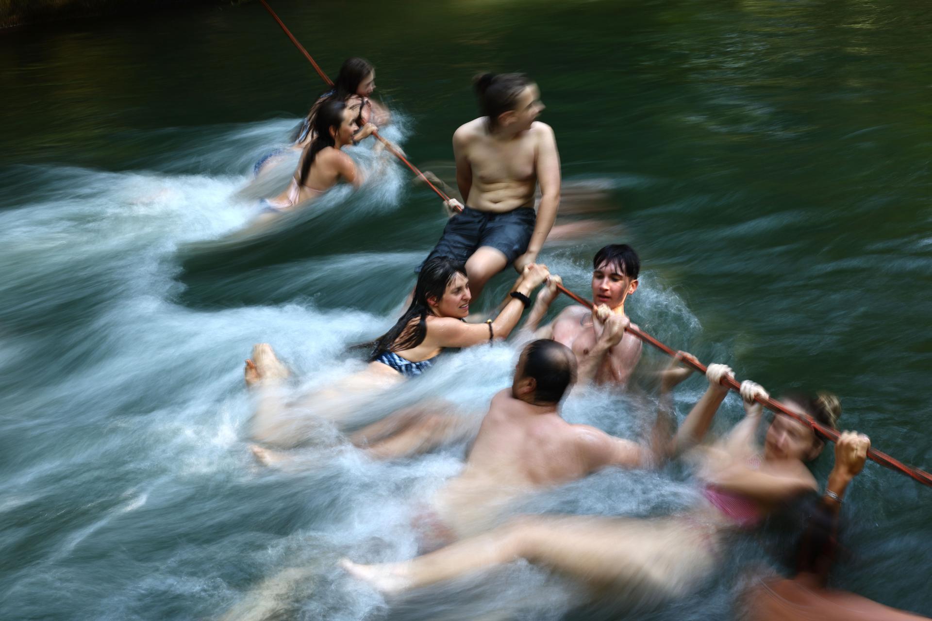 Varias personas se cuelgan de una cuerda en el arroyo Eisbach este martes, en el Jardín Inglés en Múnich (Alemania). EFE/EPA/ Anna Szilagyi