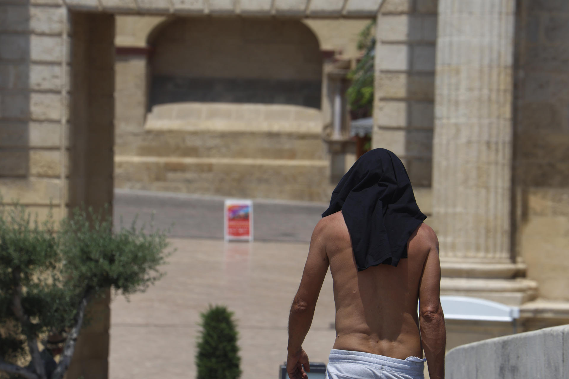 Un hombre se protege la cabeza con su camiseta, ayer martes, mientras camina por el casco histórico de Córdoba. EFE/Salas