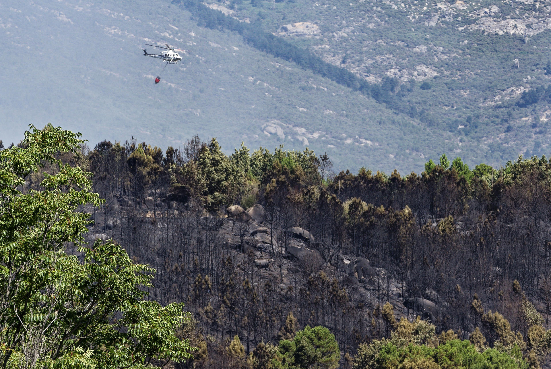 Un helicóptero de los bomberos trata de controlar el fuego declarado este martes por Mombentrán, Ávila. Un total de 101 militares y 47 medios de la Unidad Militar de Emergencias (UME) se encuentran desplegados actualmente en el Barranco de las Cinco Villas por el incendio que se declaró en la noche del lunes en esta zona del sur de la provincia de Ávila. EFE/ Raúl Sanchidrián