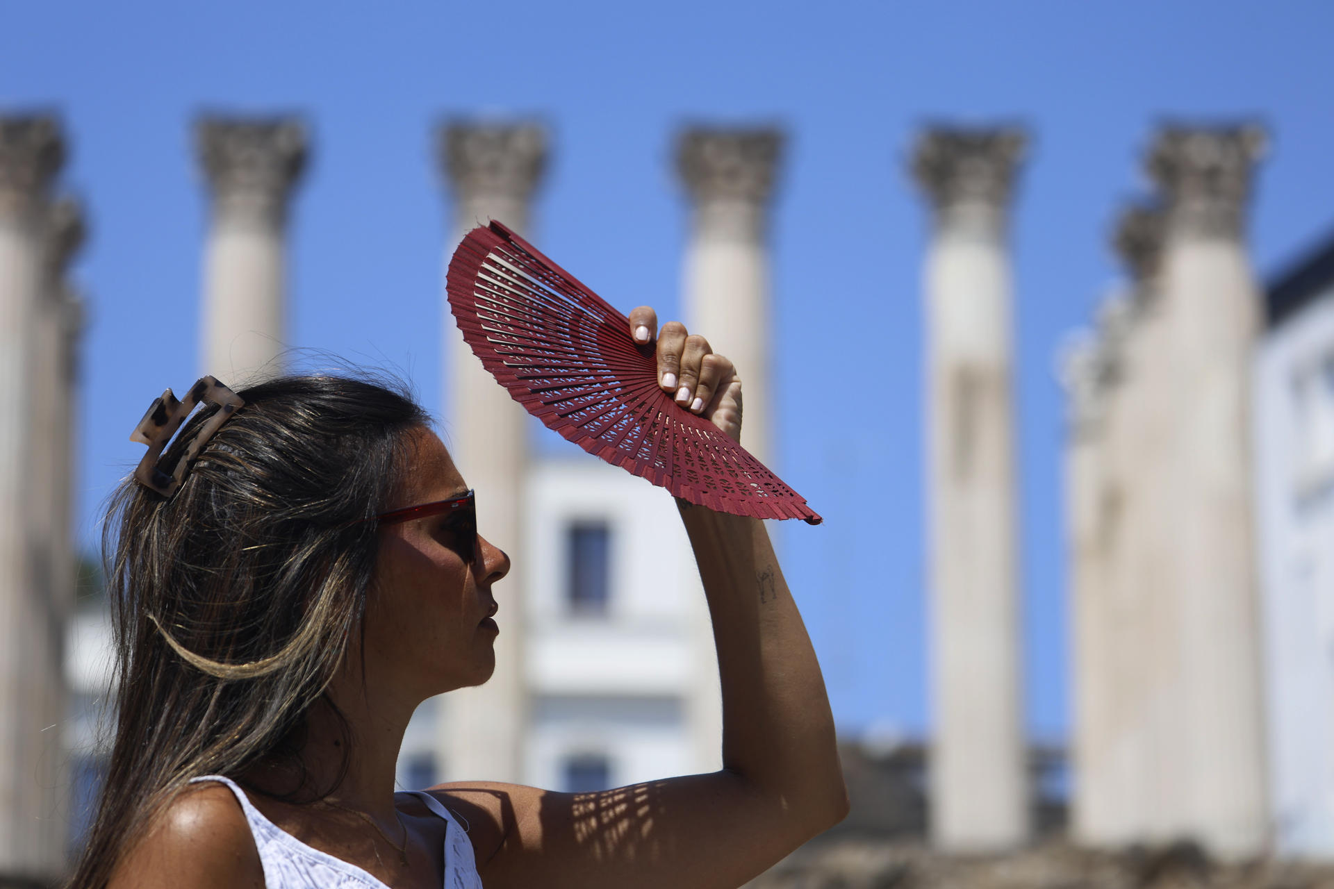 Una joven se tapa la cara con un abanico mientras camina por el centro de Córdoba este martes en el que continúa la ola de calor un día más con todo el país en alerta ante la previsión de máximas este martes de hasta 43 grados en puntos de Andalucía. EFE/Salas