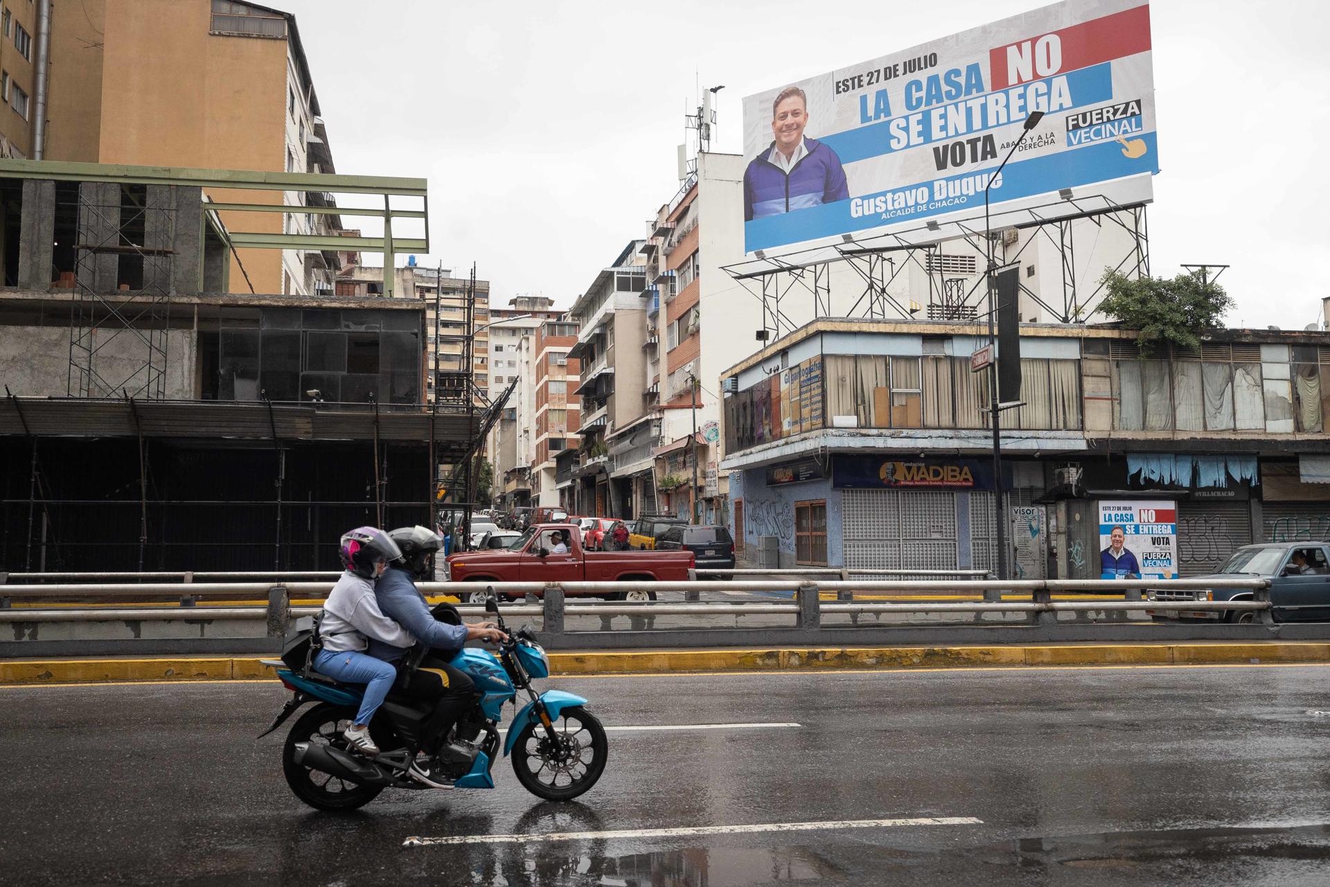 Personas en motocicleta pasan frente a un valla del alcalde del municipio Chacao de Caracas, Gustavo Duque, este sábado en Caracas (Venezuela). EFE/ Ronald Peña R