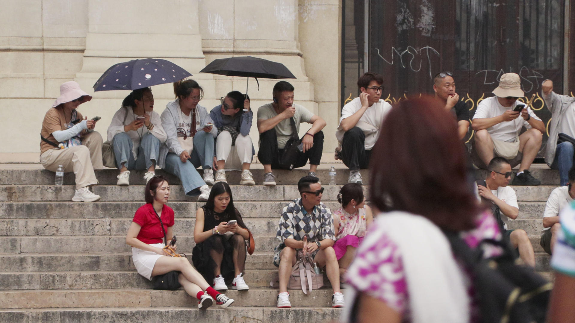 Turistas se refugian con paraguas y gorros en las escaleras de la Opéra de París, en plena ola de calor, ayer miércoles. EFE/ Edgar Sapiña