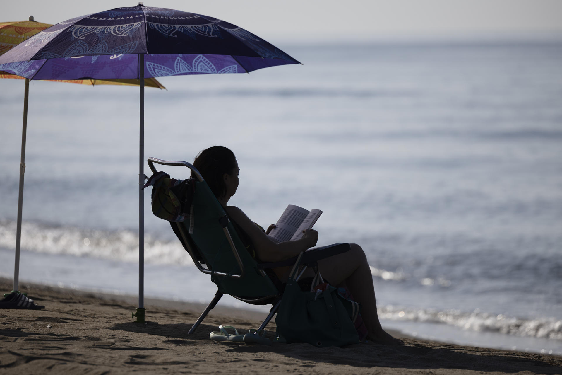 Una mujer lee bajo la sombra de una sombrilla en la playa del Rincón de la Victoria (Málaga), este miércole. EFE/Jorge Zapata