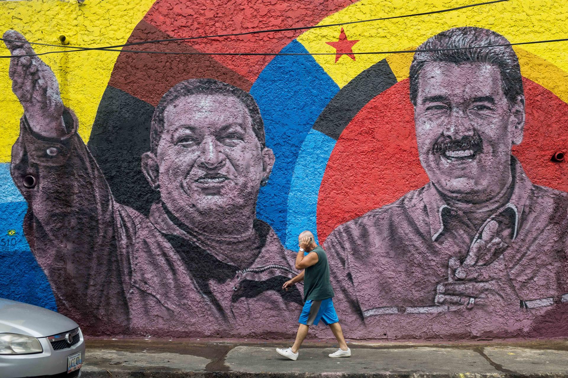 Una persona camina frente a un mural con las imagenes del presidente de Venezuela, Nicolás Maduro (d), y el fallecido presidente de Venezuela, Hugo Chavez, durante una manifestación este viernes, en Caracas (Venezuela). EFE/ Miguel Gutiérrez