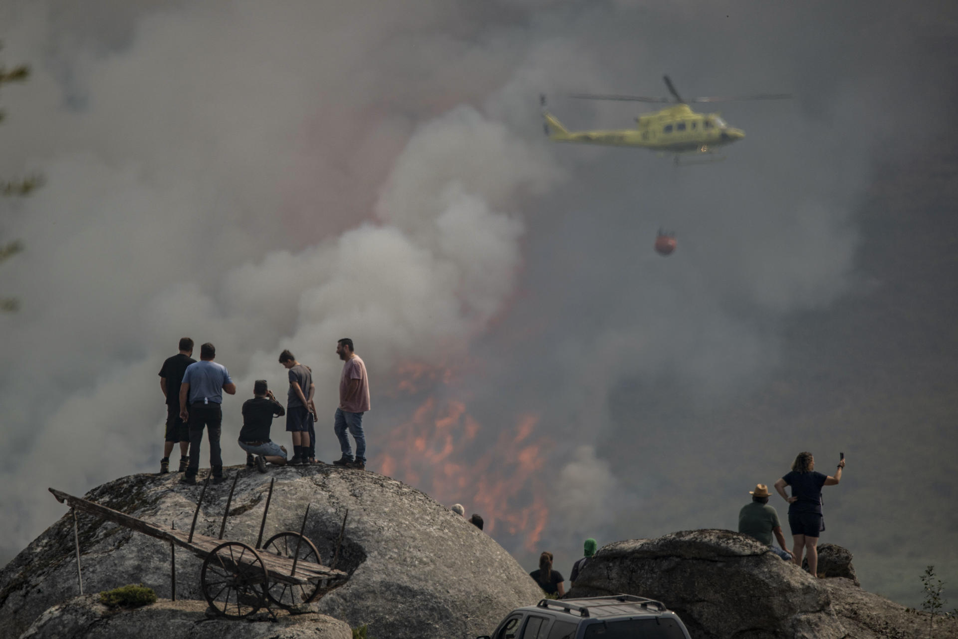 Varias personas observan la labor de un helicóptero de extinción del incendio forestal declarado ayer en Avión (Ourense), este lunes. EFE/Brais Lorenzo