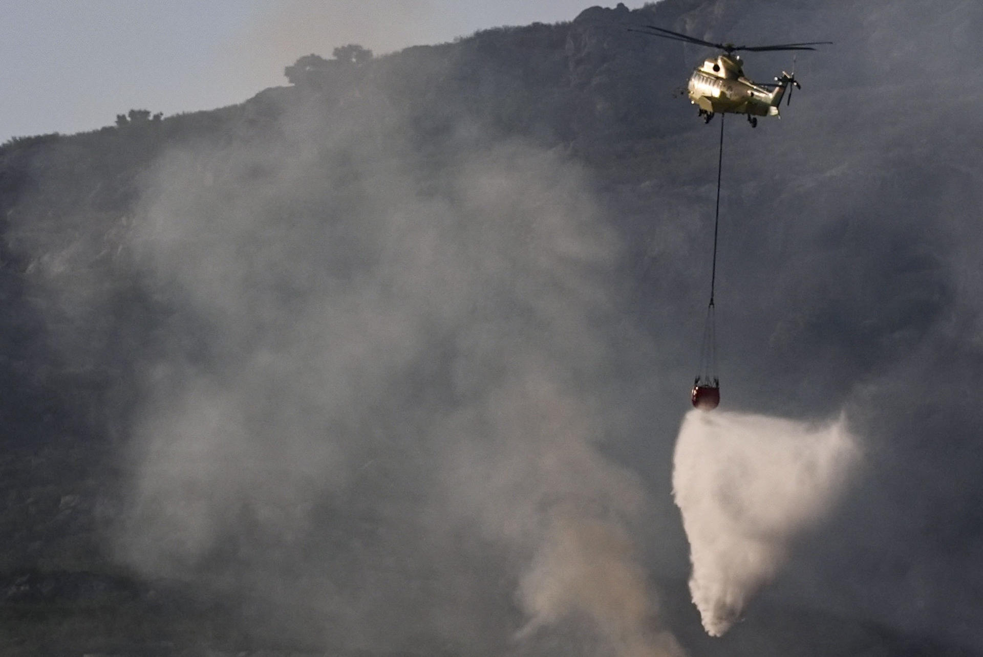 Un helicóptero trabaja en las labores de extinción del incendio que desde ayer afecta a la Sierra de la Plata, en Tarifa (Cádiz), y que sigue activo y mantiene a unas 900 personas desalojadas de sus casas y hoteles. Cuatro medios aéreos se incorporan la mañana de este martes a dichas tareas. EFE/Román Ríos