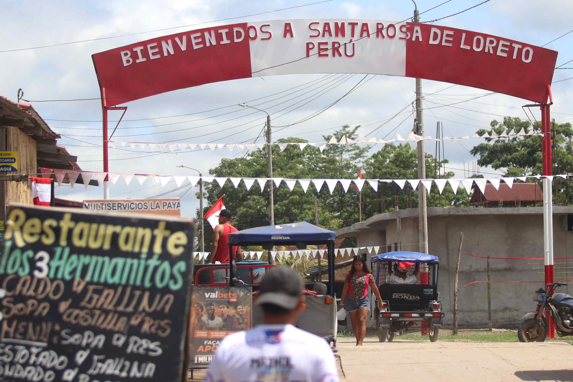 Personas se movilizan en una calle que muestra un letrero fronterizo este miércoles, en la población de Santa Rosa, una isla en medio del río Amazonas bajo soberanía peruana, situada frente a la ciudad colombiana de Leticia, en la triple frontera amazónica con Brasil. EFE/ Stringer