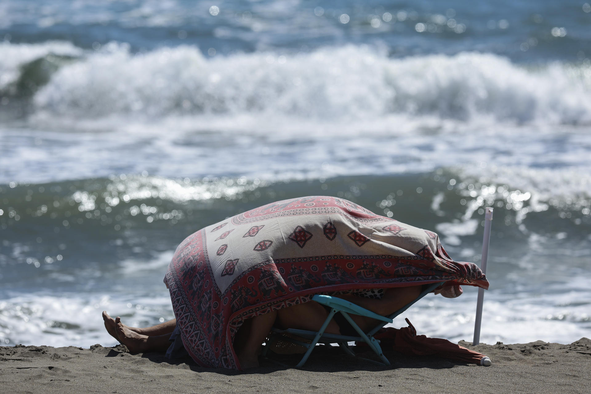 Varias personas se resguardan con una toalla del fuerte viento en la playa del Rincón de la Victoria (Málaga) este jueves. EFE/Jorge Zapata
