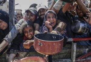 Palestinos desplazados internos, incluidos niños, sostienen ollas mientras se reúnen para recibir alimentos de un comedor benéfico en Gaza. EFE/Mohammed Saber