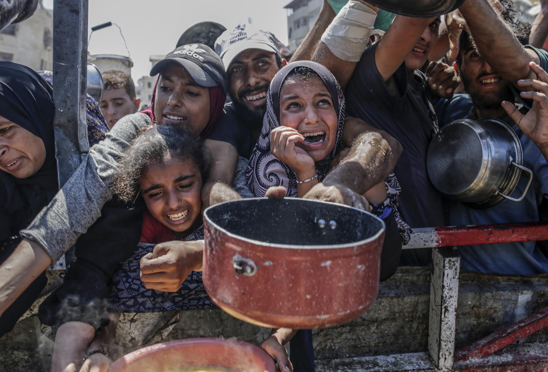 Palestinos desplazados internos, incluidos niños, sostienen ollas mientras se reúnen para recibir alimentos de un comedor benéfico en Gaza. EFE/Mohammed Saber