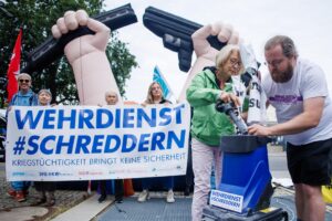 Los manifestantes rompen simbólicamente un cartel en relación con la ley del servicio militar frente a una pancarta que dice 'destruir la ley del servicio militar' con motivo de una reunión del gabinete alemán en el Ministerio de Defensa en Berlín, el 27 de agosto de 2025. EFE/EPA/CLEMENS BILAN