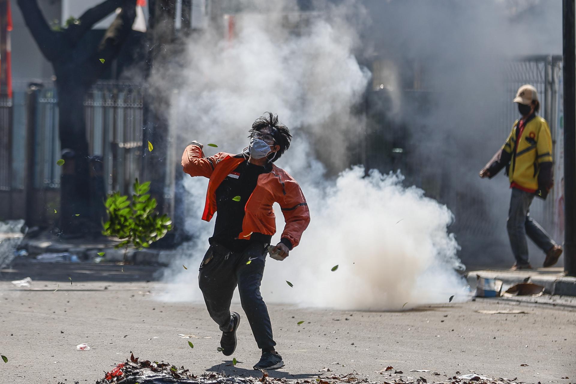 JAKARTA (Indonesia), 29/08/2025.- A protester throws a rock as a tear gas canister explodes during clashes with police outside the Mobile Brigade police headquarters in Jakarta, Indonesia, 29 August 2025. Hundreds of protesters and motorbike-hailing drivers staged a protest following the death of a motorbike-hailing driver during an earlier demonstration against the housing allowance for members of parliament. (Protestas) EFE/EPA/MAST IRHAM