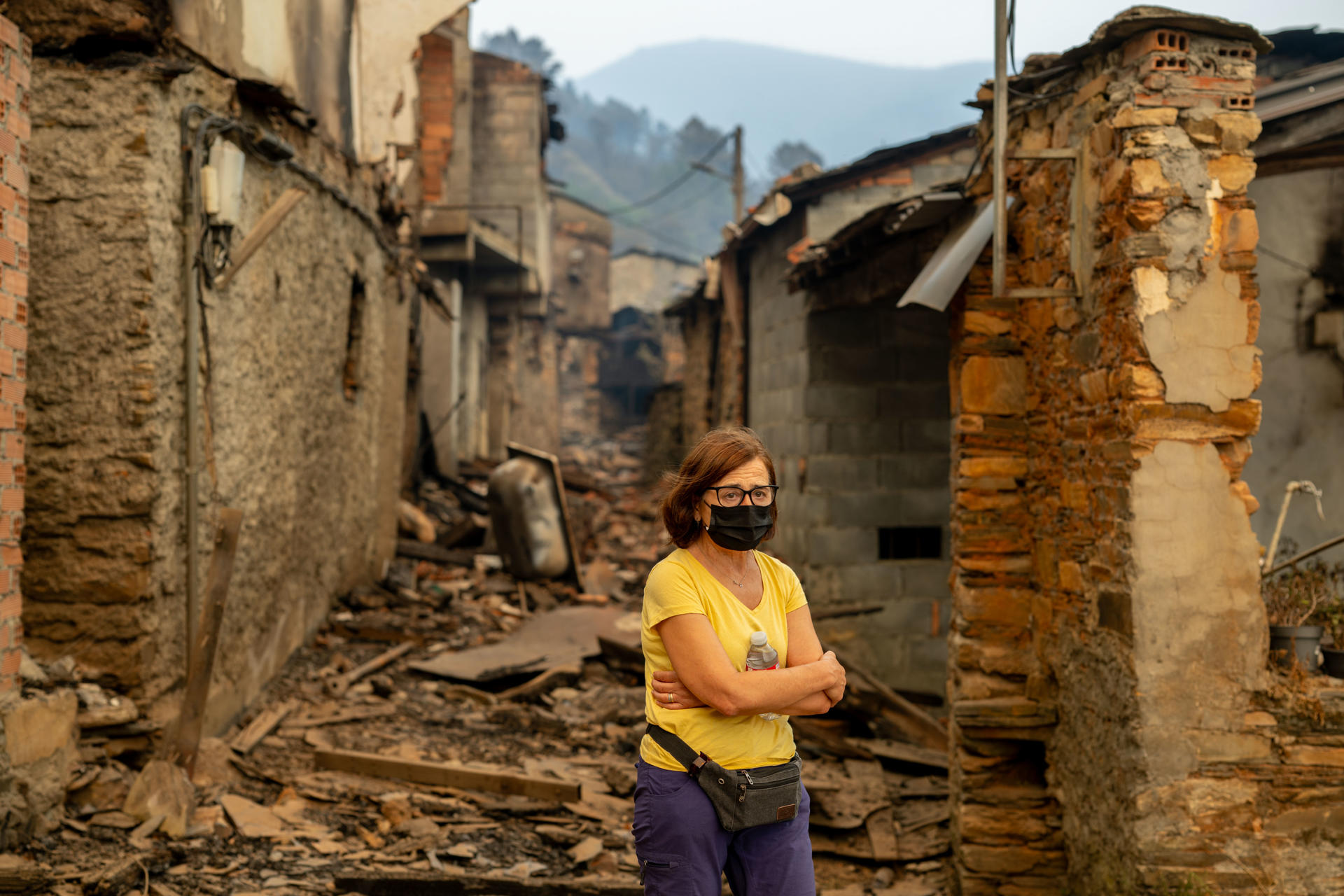 Una vecina entre las casas calcinadas de la aldea de San Vicente, este lunes en Vilamartín de Valdeorras (Ourense). EFE/ Brais Lorenzo