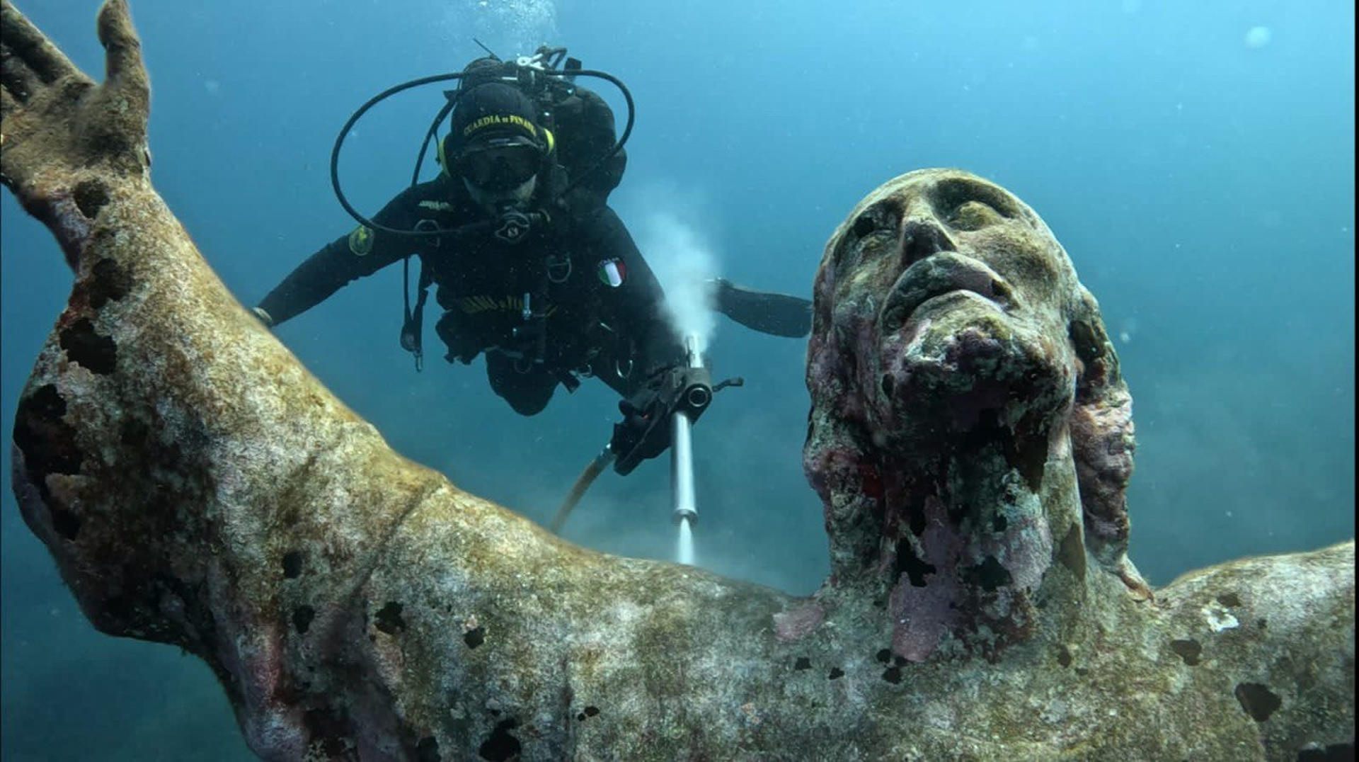La estatua del Cristo de los Abismos, ubicada a 17 metros de profundidad en el fondo marino de la bahía de San Fruttuoso, en la costa de Liguria (norte de Italia), ha sido sometida a su limpieza anual por un equipo de buzos especializado. Obra del escultor Guido Galletti, la escultura de bronce, que mide 2,5 metros de altura y pesa 250 kilogramos, fue colocada en el fondo marino en 1954 y representa a Cristo con los brazos extendidos y la mirada dirigida hacia la superficie en homenaje a las vidas perdidas en el mar. EFE/Guardia de Finanzas de Italia  SOLO USO EDITORIAL/SOLO DISPONIBLE PARA ILUSTRAR LA NOTICIA QUE ACOMPAÑA (CRÉDITO OBLIGATORIO)