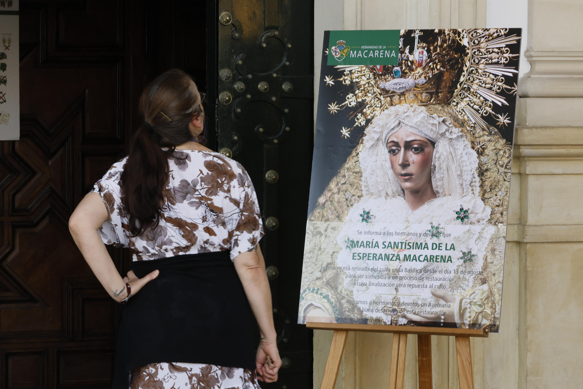 Una mujer lee el cartel con la imagen de la Esperanza Macarena en la basílica de Sevilla en el que se informa de su restauración tras ser retirada. EFE /José Manuel Vidal

