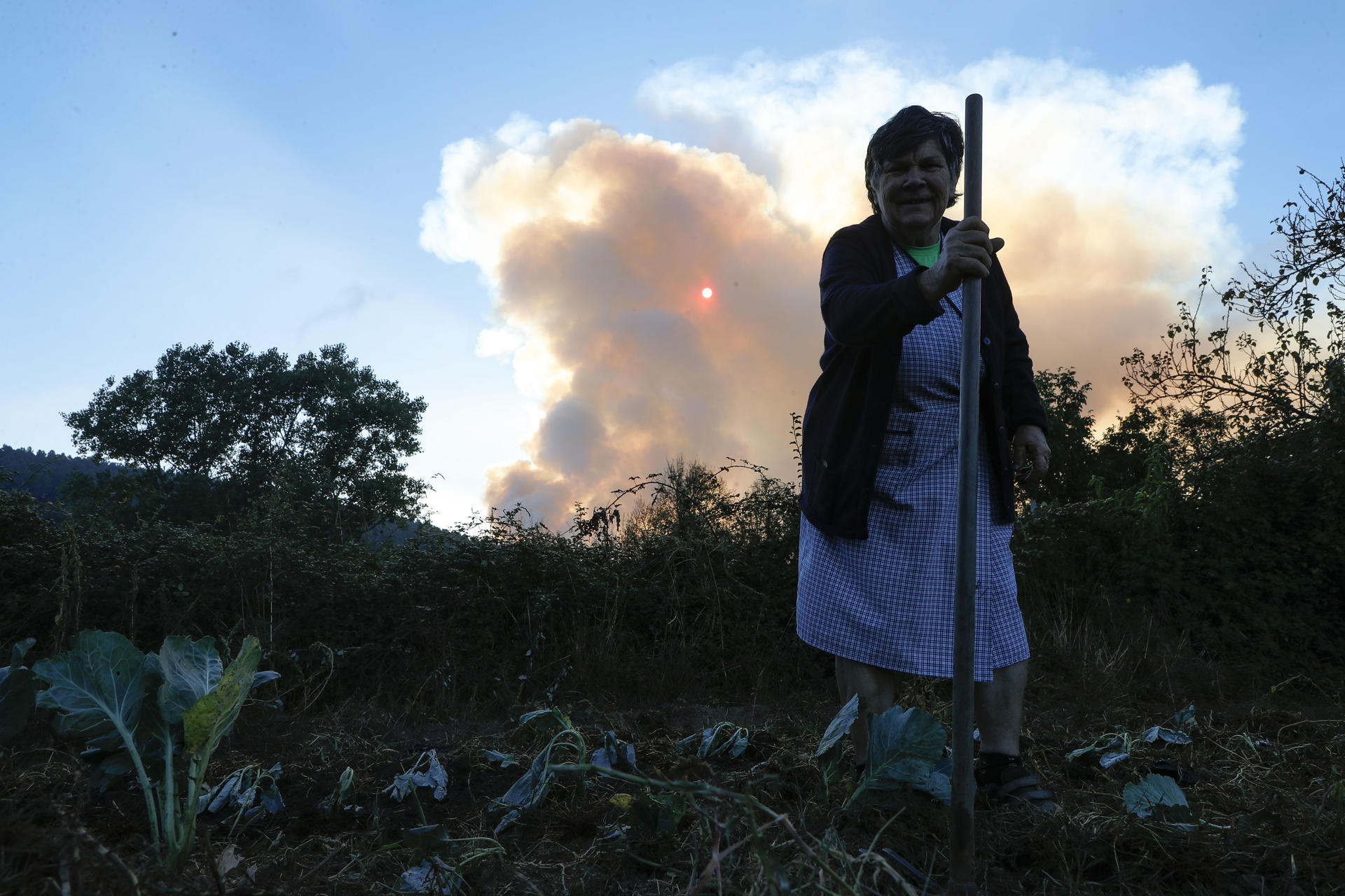 Una mujer mira la columna de humo desde un pueblo en Pobra de Brollón, Lugo. EFE/ Eliseo Trigo