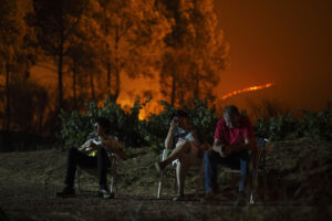 Una familia en el exterior de su vivienda, que ha quedado rodeada por el fuego, en el incendio forestal de A Rúa (Ourense). EFE/ Brais Lorenzo