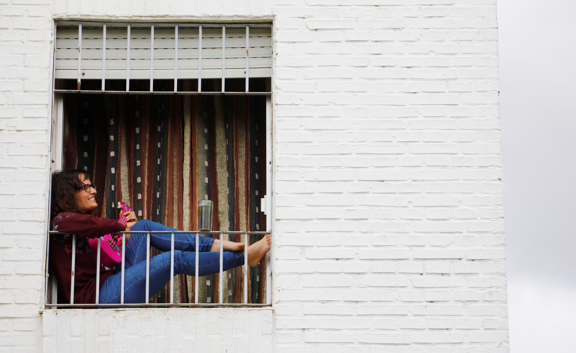 Una joven toca una guitarra sentada en la ventana de su vivienda en Córdoba, en una imagen de archivo. EFE/Salas