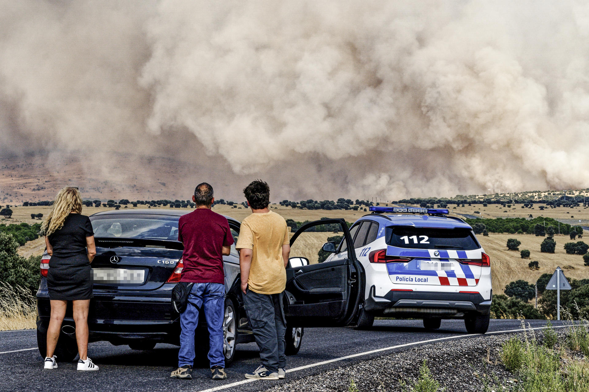 Un grupo de personas paradas en la carretera AV-500, la cual se encuentra cortada en las proximidades de Urraca-Miguel, barrio anexionado de Ávila capital con motivo del incendio que azota la zona este viernes. EFE/ Raúl Sanchidrián
