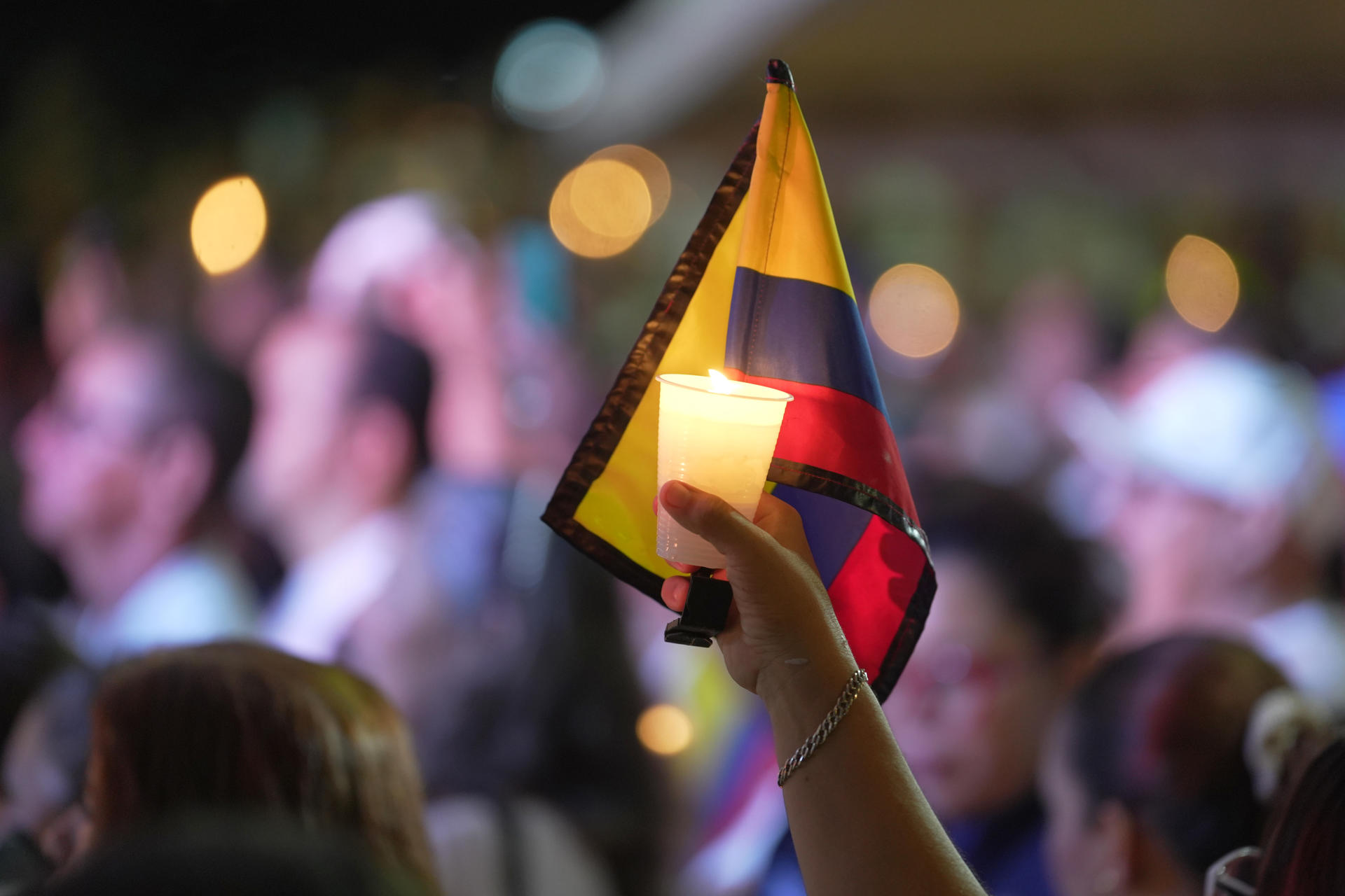 Detalle de la mano de una persona al sostener una vela encendida y una bandera de Colombia, durante una 'velatón' por la paz y la memoria, frente a la Base Aérea Marco Fidel Suárez, que fue atacada con un carro bomba el pasado día 21, en Cali (Colombia). EFE/Ernesto Guzmán
