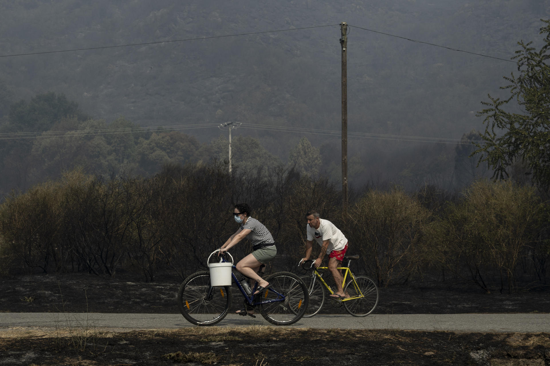 Dos personas, una de ellas protegida con una mascarilla, circulan en bicicleta por una zona quemada debido al incendio de Monterrei (Ourense). EFE /Brais Lorenzo
